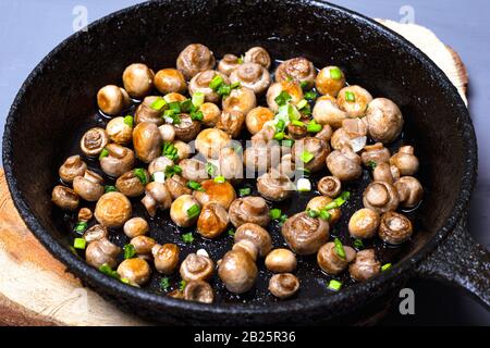 campaignoni di funghi fritti con cipolle verdi in una padella in ghisa su un supporto in legno. Foto Stock
