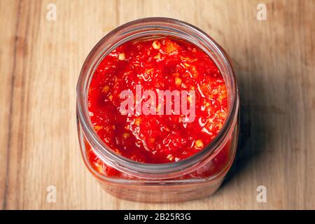 vasetto con peperoncino rosso e salsa di pomodoro. Salsa jadika tradizionale caucasica su tavola di legno. Foto Stock