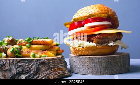 gustoso hamburger con verdure a cotoletta di carne e formaggio con morbido panino, patatine fritte e funghi champignon cosparsi di cipolle verdi sulla foresta coa di legno Foto Stock