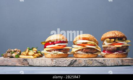 hamburger succosa con patate fritte e funghi su un piatto di legno. hamburger con formaggio a taglio e verdure su sfondo grigio. Foto Stock