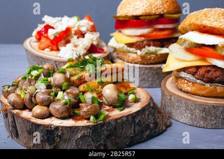 patate fritte con funghi e hamburger di carne succosa su monconi di legno su sfondo grigio. fast food forest. Foto Stock