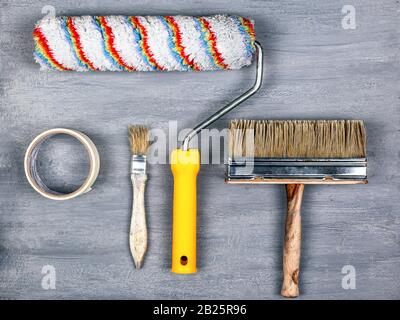 concetto di lavoro di pittura. set di utensili per la verniciatura e la riparazione di pareti. rullo e pennello su sfondo grigio. Foto Stock