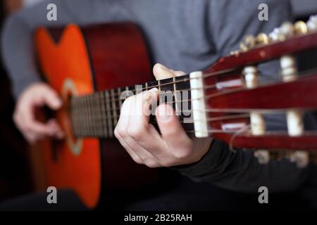 l'uomo suona con una chitarra arancione acustica. l'arte di suonare uno strumento musicale classico a corde. Foto Stock