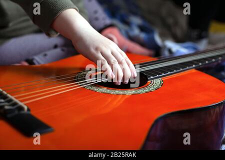 la mano dei bambini tira le corde su una chitarra acustica arancione. Foto Stock