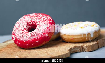 Ciambelle multicolori assortiti rosso, bianco, viola rivestite con smalto e cosparse di polvere di Pasqua su un supporto in legno su sfondo grigio, dolce eco foo Foto Stock