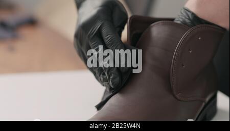 uomo mani in guanti neri applicando crema protettiva a stivali chukka in pelle marrone, foto larga Foto Stock