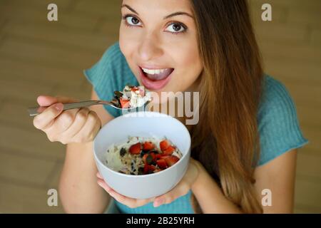 Vista ravvicinata dall'alto della bella giovane donna che mangia il cielo con cereali muesli frutta e semi a casa, concentrarsi su modelli di occhi indoor shot. Sano foo Foto Stock