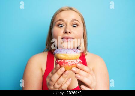 Fat ragazza pensa di mangiare ciambelle invece di fare palestra. Concetto di indecisione e dubbio Foto Stock