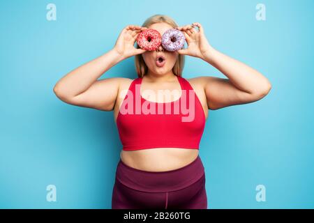 Fat ragazza pensa di mangiare ciambelle invece di fare palestra. Concetto di indecisione e dubbio Foto Stock