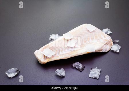 Filetto di pollock congelato con pezzi di ghiaccio. Concetto di pesce sano. Pesce organico su uno sfondo di pietra nera, copia spazio Foto Stock