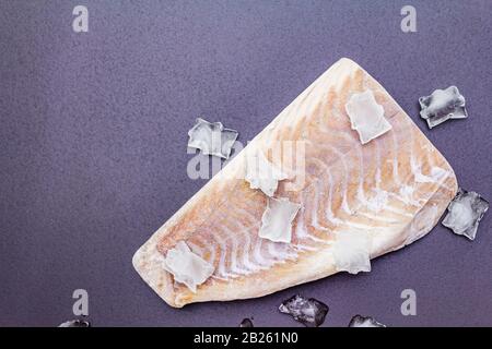 Filetto di pollock congelato con pezzi di ghiaccio. Concetto di pesce sano. Pesce organico su uno sfondo di pietra nera, copia spazio, vista dall'alto Foto Stock