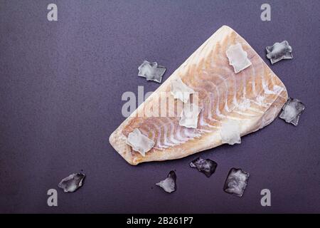 Filetto di pollock congelato con pezzi di ghiaccio. Concetto di pesce sano. Pesce organico su uno sfondo di pietra nera, copia spazio, vista dall'alto Foto Stock