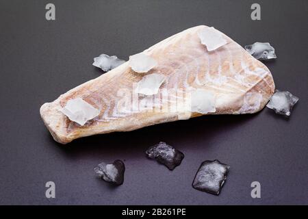 Filetto di pollock congelato con pezzi di ghiaccio. Concetto di pesce sano. Pesce organico su uno sfondo di pietra nera. Foto Stock