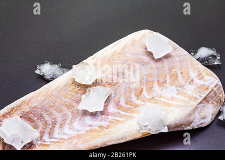 Filetto di pollock congelato con pezzi di ghiaccio. Concetto di pesce sano. Pesci organici su uno sfondo di pietra nera, primo piano Foto Stock