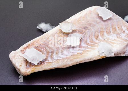 Filetto di pollock congelato con pezzi di ghiaccio. Concetto di pesce sano. Pesci organici su uno sfondo di pietra nera, primo piano Foto Stock