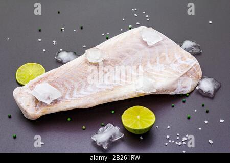 Filetto di pollock congelato con pezzi di ghiaccio. Concetto di pesce sano. Pesci organici su uno sfondo di pietra nera, primo piano Foto Stock