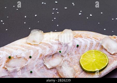 Filetto di pollock congelato con pezzi di ghiaccio. Concetto di pesce sano. Pesci organici su uno sfondo di pietra nera, primo piano Foto Stock