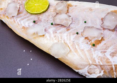 Filetto di pollock congelato con pezzi di ghiaccio. Concetto di pesce sano. Pesci organici su uno sfondo di pietra nera, primo piano Foto Stock