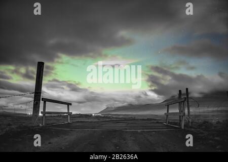 Aurora in Islanda luci settentrionali che brillano attraverso le lacune nelle nuvole sopra la porta fattoria islandese in bianco nero e verde Foto Stock