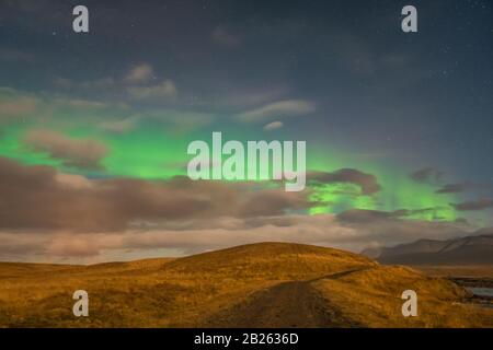 Aurora in Islanda luci settentrionali fasci luminosi sopra le nuvole durante la luna piena Foto Stock