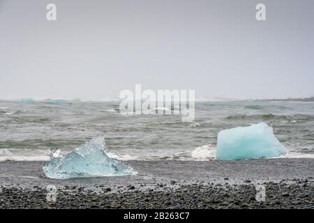 Spiaggia di diamanti sabbia nera cristallo blu chiaro pezzi di ghiaccio sulla spiaggia e sul mare Foto Stock