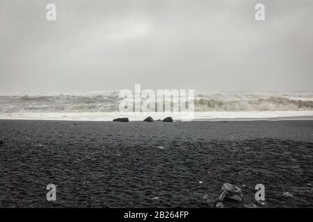 Spiaggia di Reynisfjara vicino a Reynisdrangar enormi onde che colpiscono la spiaggia durante il tempo tempestoso e la pioggia pesante Foto Stock