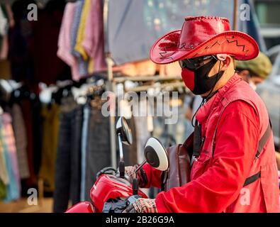 Uomo su una motocicletta che indossa un cappello rosso e una maschera di faccia rossa. Foto Stock