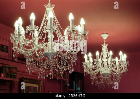 Lampadari bianchi in cristallo finto e candele appesi a un soffitto dipinto di rosso Foto Stock