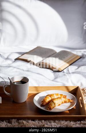 Cornetti francesi e caffè nero sul vassoio in camera da letto a colazione Foto Stock