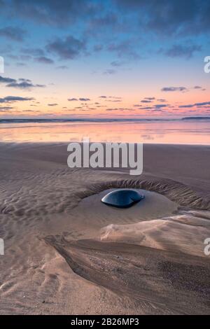 Lone ghiaia nella piscina di roccia con il cielo del tramonto e orizzonte maledetto sulla spiaggia a Westward ho!, North Devon, South West, UK Foto Stock