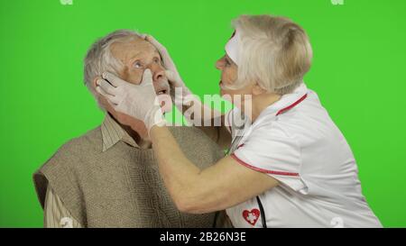 Gentile donna matura infermiere assistenza per anziani aiutare con il problema, medico terapista femminile in uniforme esamina l'uomo e dare suggerimenti per il trattamento di pazienti anziani Foto Stock