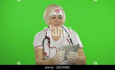 Ritratto di anziano medico caucasico femmina riceve denaro. Conta soldi. Infermiera femminile. Schermo verde. Tasto Chroma Foto Stock