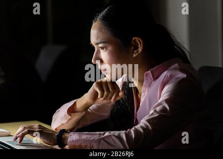Giovane donna d'affari asiatica che lavora sodo e tardi di notte nel suo ufficio con computer portatile. Utilizzo come duro lavoro e lavorare in ritardo concetto. Foto Stock