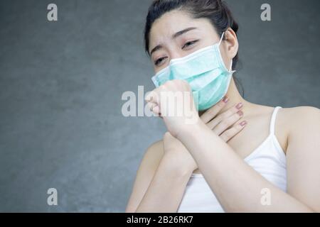 Una donna asiatica che ha un freddo e tosse. Ragazza con maschera protettiva o Igienica in piedi per Virus su sfondo grigio chiaro parete. Spazio di copia. Ilne Foto Stock