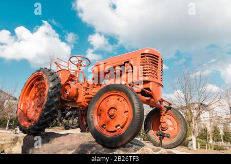 vecchio trattore rosso in fattoria su cielo blu con nuvole Foto Stock