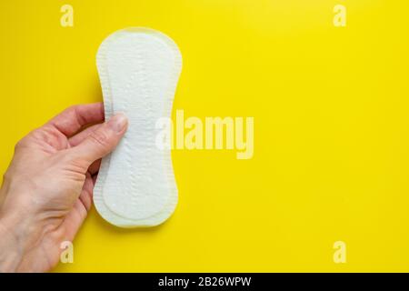 Mano della donna che tiene un assorbente igienico quotidiano su uno sfondo giallo luminoso primo piano dello spazio della copia Foto Stock