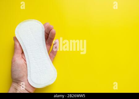 Mano della donna che tiene un assorbente igienico quotidiano su uno sfondo giallo luminoso primo piano dello spazio della copia Foto Stock