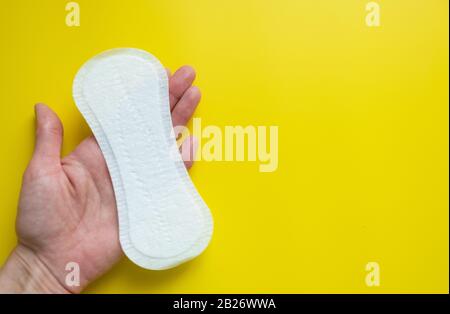 Mano della donna che tiene un assorbente igienico quotidiano su uno sfondo giallo luminoso primo piano dello spazio della copia Foto Stock