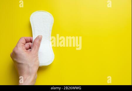 Mano della donna che tiene un assorbente igienico quotidiano su uno sfondo giallo luminoso primo piano dello spazio della copia Foto Stock