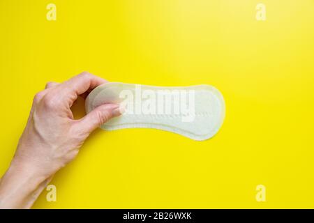 Mano della donna che tiene un assorbente igienico quotidiano su uno sfondo giallo luminoso primo piano dello spazio della copia Foto Stock