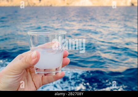 Persona turistica tenere un bicchierino di vetro di Ouzo strega è un aperitivo secco al gusto di anice e la degustazione all'aperto a Santorini, Grecia. Foto Stock