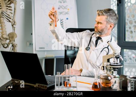 Medico scienziato maschio concentrato caucasico che lavora in laboratorio, facendo ricerche e facendo esperimenti, tenendo provetta con nuovo campione di vaccino o farmaco Foto Stock