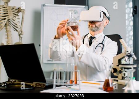 Medico caucasico, scienziato, virologo, indossando occhiali per la realtà virtuale per l'immaginazione, conducendo ricerche in laboratorio, tenendo fiasca Foto Stock