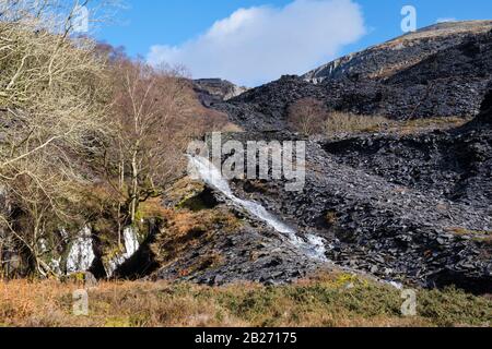 Ruscello e scorie mucchi in cava di ardesia Dinorwig sotto Elidir Fawr montagna. Dinorwic, Llanberis, Gwynedd, Galles del Nord, Regno Unito, Gran Bretagna Foto Stock