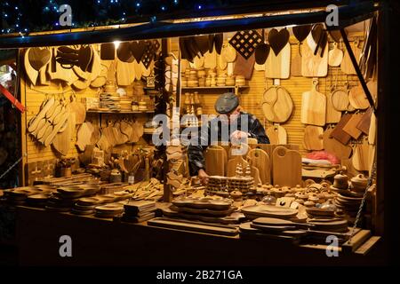 Uomo che vende utensili da cucina tradizionali in legno al mercatino di Natale di notte, a Varsavia, Polonia Foto Stock