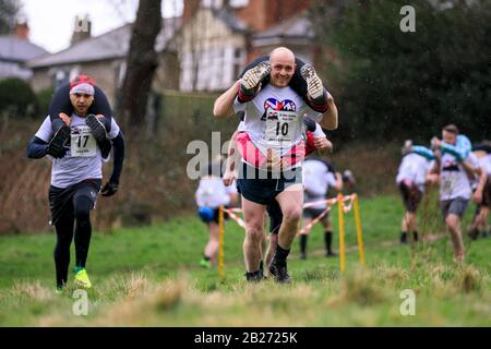 James Holden e Rose Holden da Manchester (a destra) hanno ritratto all'annuale Moglie Che Porta Race a Dorking, Surrey. I corridori competono su un percorso di 380m, con 15m di salita e 15m di discesa. Foto Stock