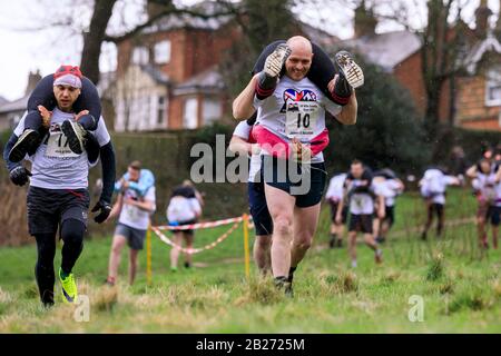 James Holden e Rose Holden da Manchester (a destra) hanno ritratto all'annuale Moglie Che Porta Race a Dorking, Surrey. I corridori competono su un percorso di 380m, con 15m di salita e 15m di discesa. Foto Stock