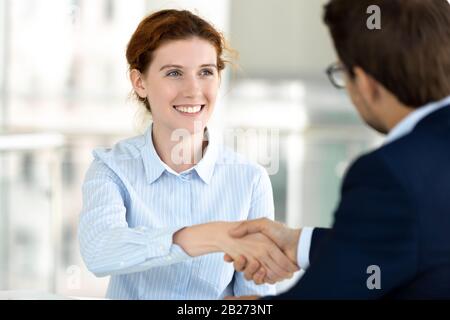 Primo piano sorridente attraente donna handshaking con capo durante la riunione. Foto Stock
