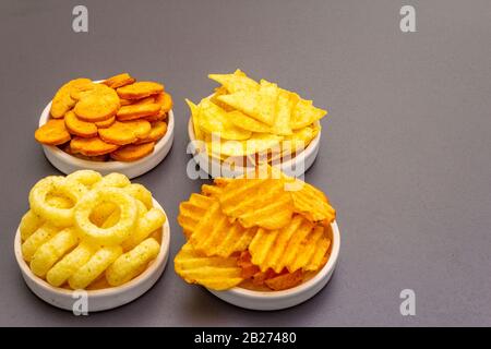 Spuntini salati speziati assortiti. Patatine, anelli, nachos, cracker. In ciotole di ceramica su uno sfondo di pietra Foto Stock