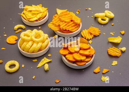 Spuntini salati speziati assortiti. Patatine, anelli, nachos, cracker. In ciotole di ceramica su uno sfondo di pietra Foto Stock